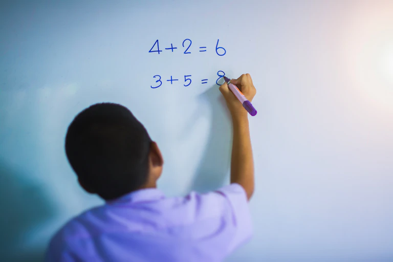 A young child does simple sums on a whiteboard.