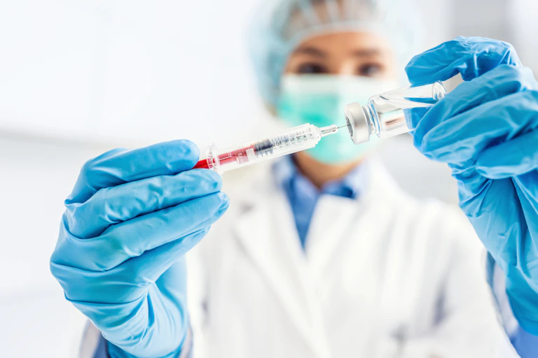 Une médecin, avec masque, gants et charlotte, remplit sa seringue avant injection