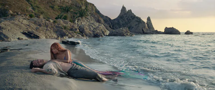 Halle Bailey and Jonah Hauer-King lying washed up on the short, Bailey as a mermaid.
