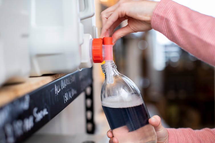 A person fills a glass container with cleaning fluid from a container on a shelf.