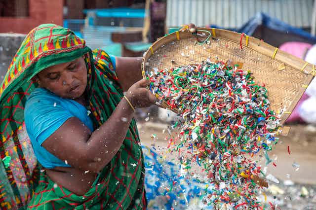 A person sorts colourful plastic fragments using a rattan scoop.