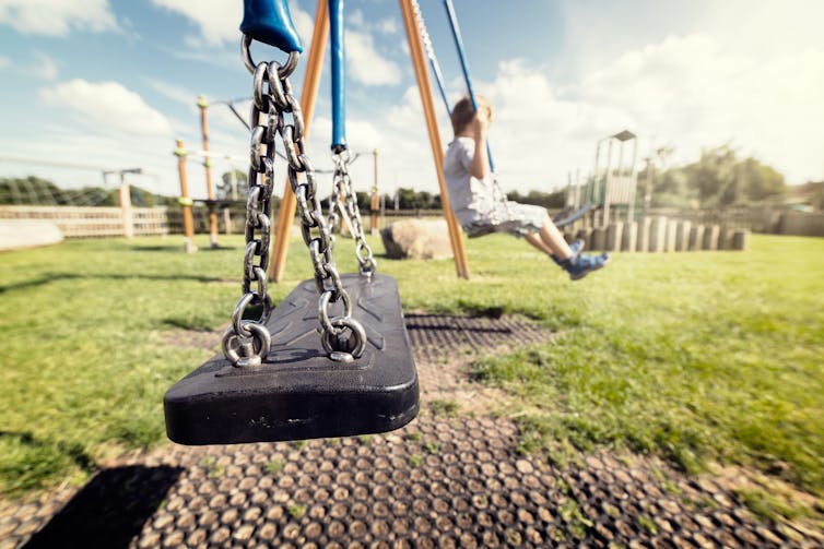 A child on a swing in a sunny but empty playground