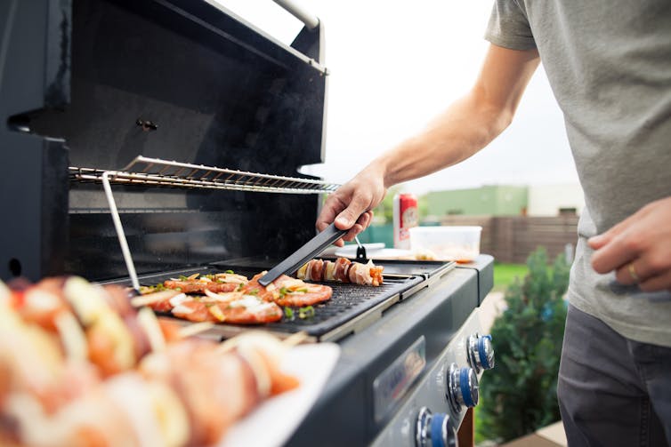 Hand of young man grilling some meat and vegetable skewers on a gas grill.