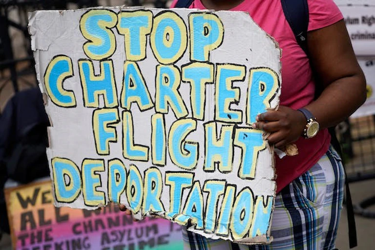 Une femme tient une pancarte sur laquelle est écrit "stop aux expulsions par vol charter".