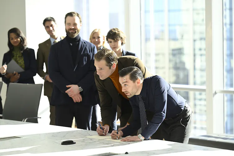 Roman and Matson sign papers in a large boardroom