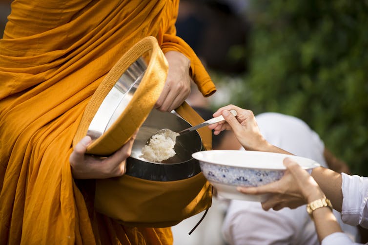A person putting cooked rice in the alms bowl of a Buddhist monk.