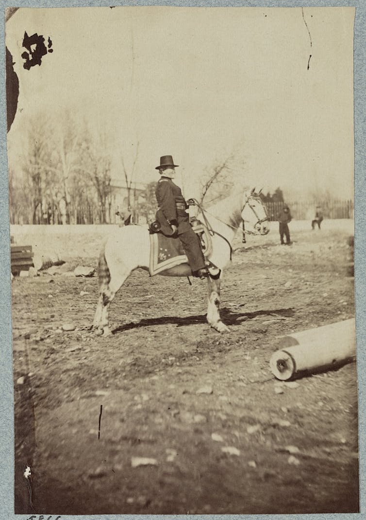A man wearing a Union Army uniform sits atop a horse in the middle of a field.