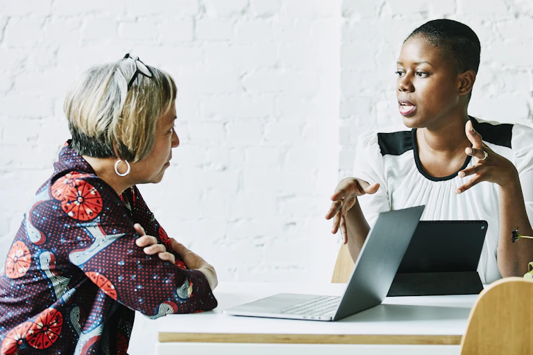 two women at table with laptops in discussion