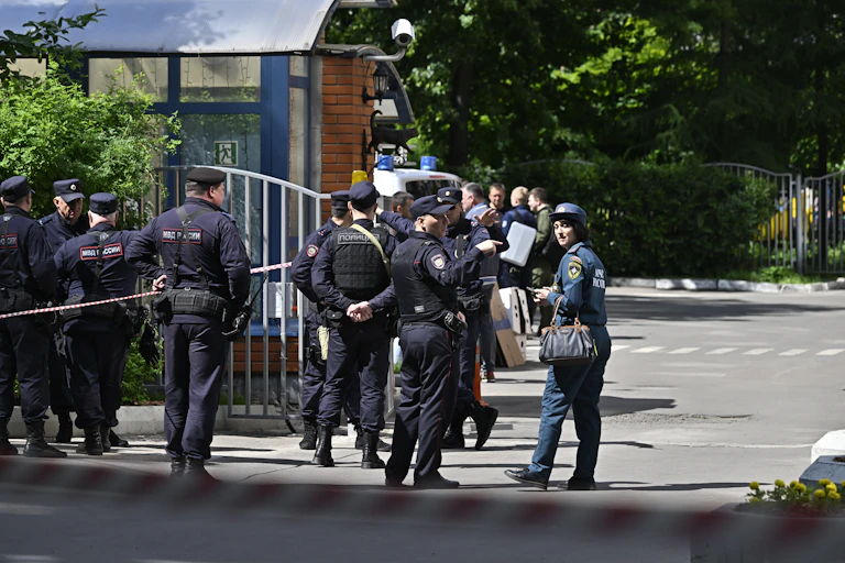 A group of police officers in dark blue gather together on a quiet street in front of trees.