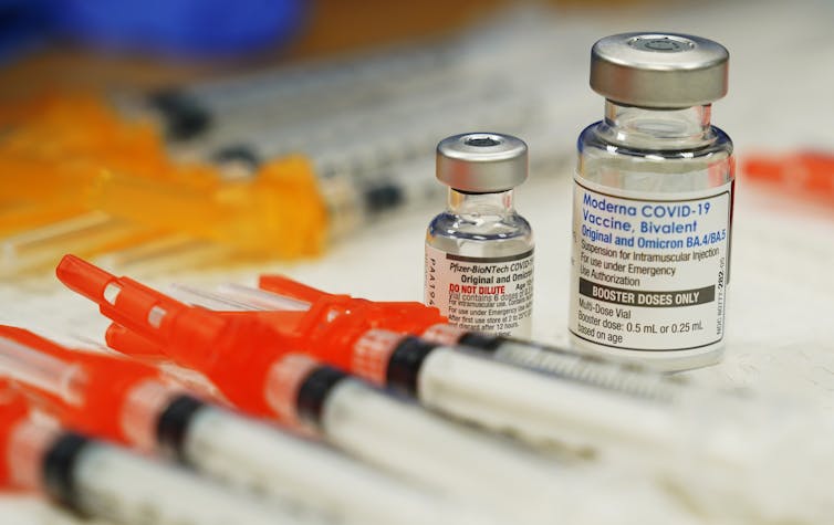 Syringes lined up in front of two vials of vaccine