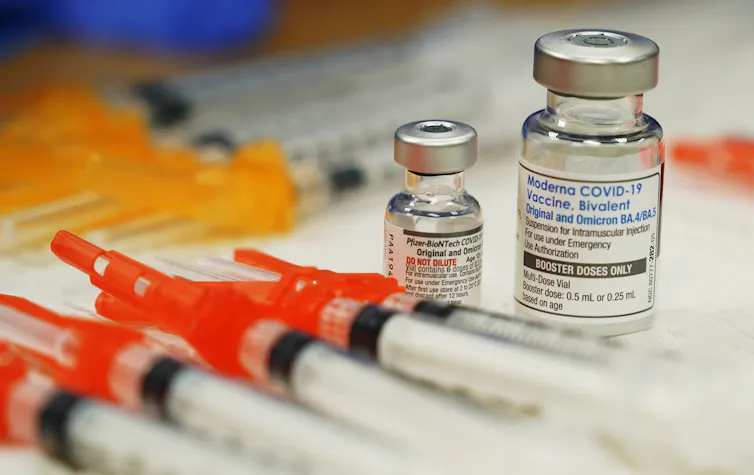 Syringes lined up in front of two vials of vaccine