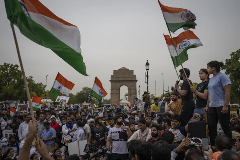 People march down a street waving Indian flags.