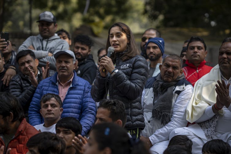 A woman holding a microphone speaks to people at a protest.
