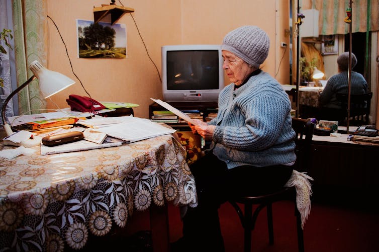 Older woman wearing a beanie sorts papers in her living room