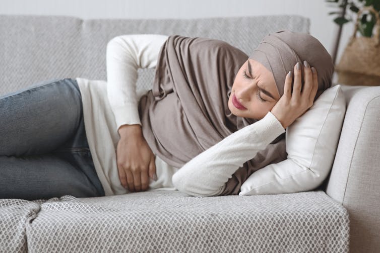 Woman clutching tummy and head lying on sofa