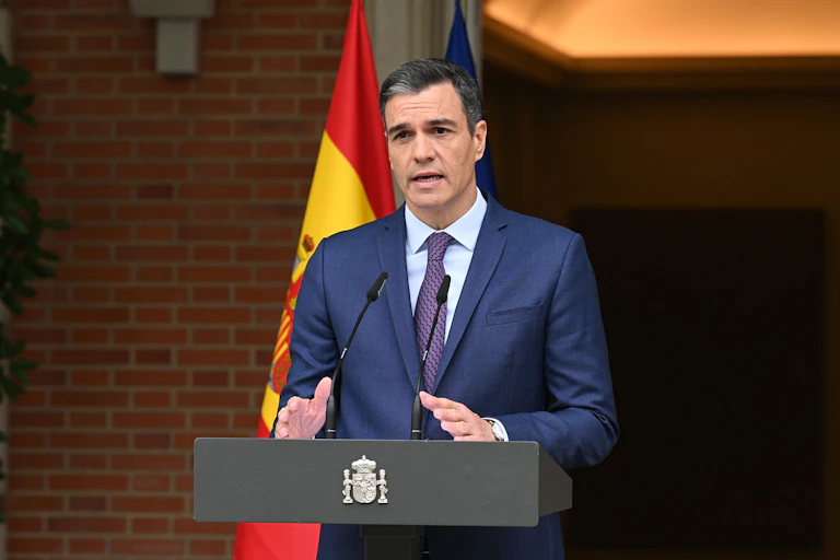 A man in front of a building with a flag standing behind him makes an announcement.