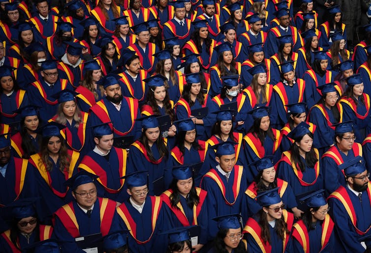 A sea of university graduates in their convocation robes and caps inside an auditorium.