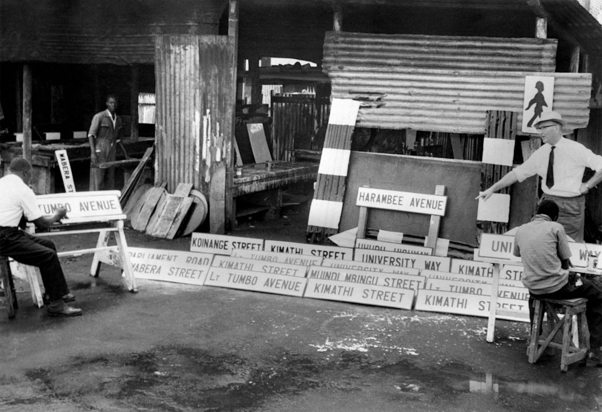 A black and white photo with signwriters painting street names on street signs