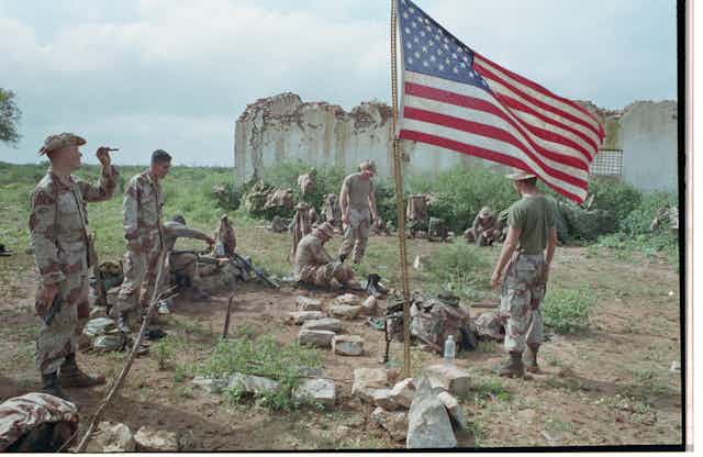 A group of men wearing fatigues are gathered around an American flag.