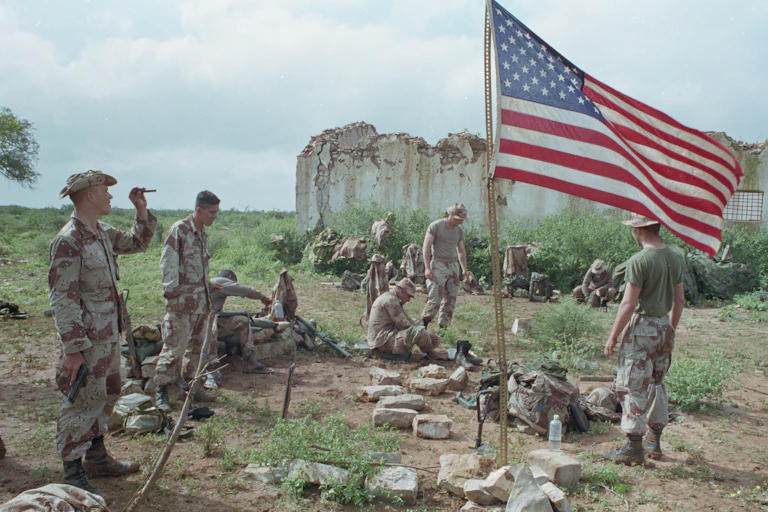 A group of men wearing fatigues are gathered around an American flag.