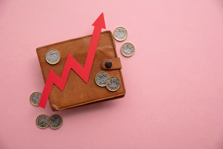 Wallet surrounded by pound coins, red arrow pointing upwards, pink background.