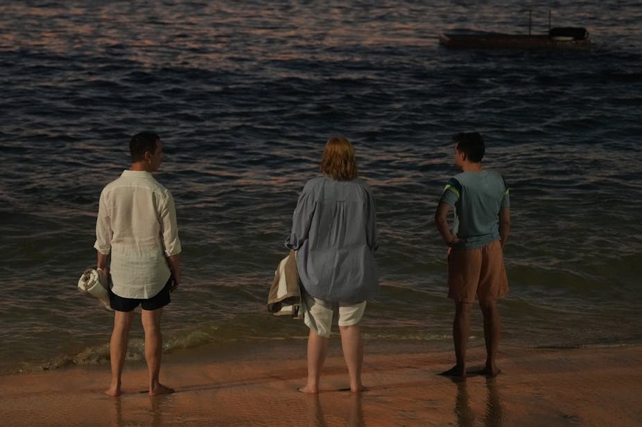 Jeremy Strong, Sarah Snook and  Kieran Culkin stand on a beach looking out to sea, shot from behind.