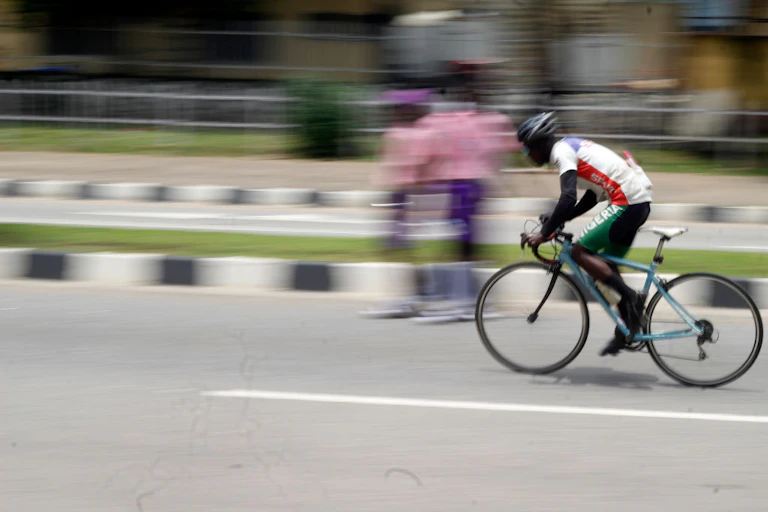 A man rides a bicycle on a street, passing pedestrians who are in a blur