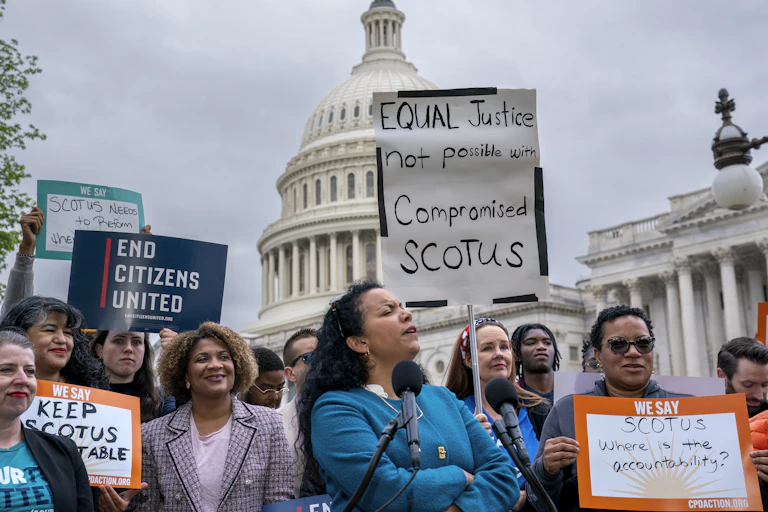 About a dozen people demonstrating outside of a white-domed US Capitol building, with signs that say 'End Citizens United' and 'Keep SCOTUS accountable,' among others.
