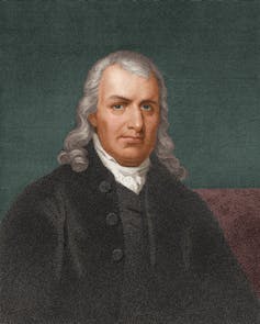 A middle-aged man from an earlier century dressed in a black robe and with long gray hair.