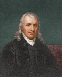 A middle-aged man from an earlier century dressed in a black robe and with long gray hair.