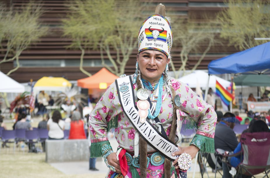 A person in brightly colored dress, wearing a sash that says 'Miss Montana Two-Spirit.'