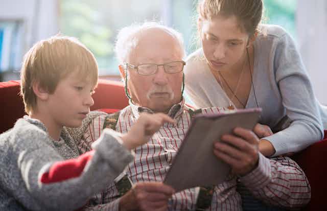 A young boy, elderly man, and a woman sit on a couch using an ipad.