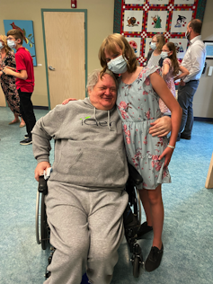 A girl and an elderly man in a wheelchair pose for a photo together.