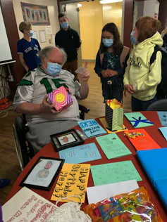 A man in wheelchair receives birthday cards from young children.