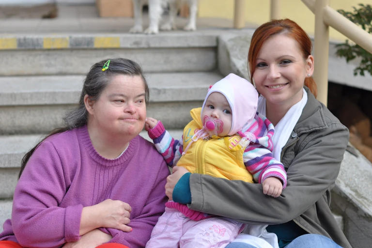 Woman with Down's syndrome sitting on outside step with other woman, young child on lap