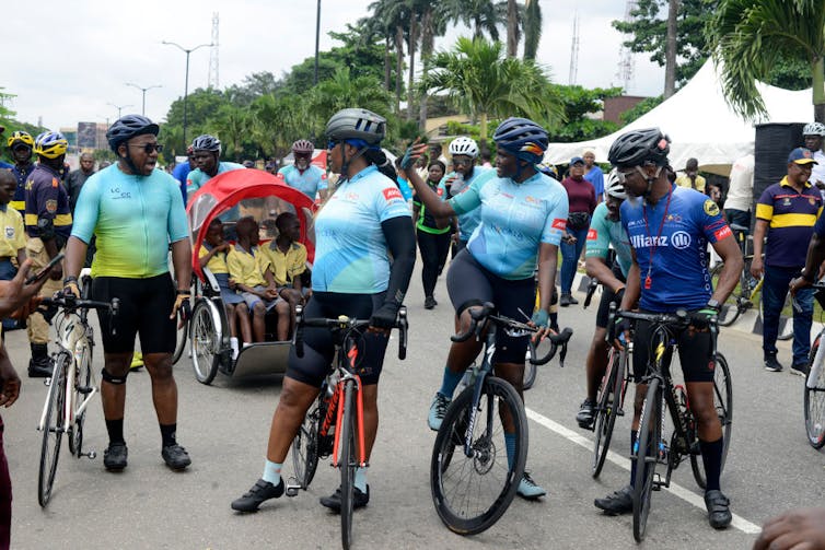 A group of people chat, on or next to their bicycles, wearing cycling gear and helmets.