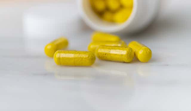 Pill bottle on side containing yellow capsules, some spilling on table or countertop