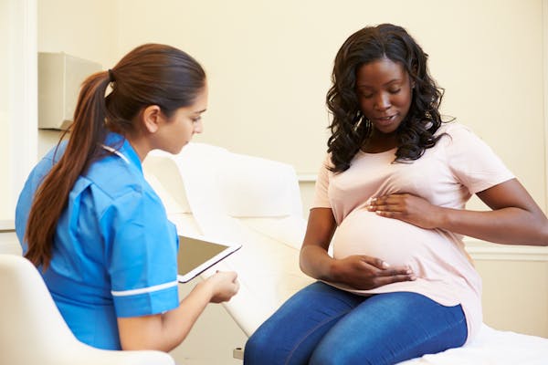 An expectant mother cradles her stomach while speaking with her doctor.