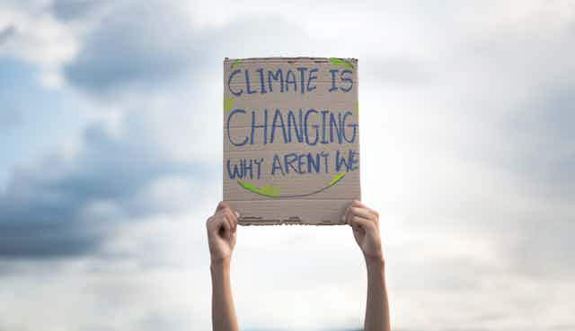 Manos sostienen en alto una pancarta que dice "Climate is changing, why aren't we".