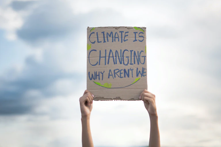 Manos sostienen en alto una pancarta que dice "Climate is changing, why aren't we".