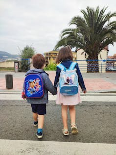 Niños de espaldas, de la mano, caminando con mochilas.