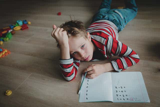 Un niño tumbado en el suelo desesperado mientras hace deberes de matemáticas.