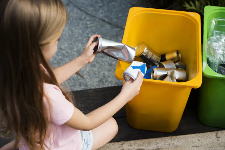 Anak perempuan menyortir kaleng ke dalam tempat sampah daur ulang
