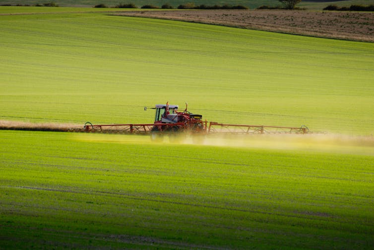 A tractor with outspread spraying arms in a field.