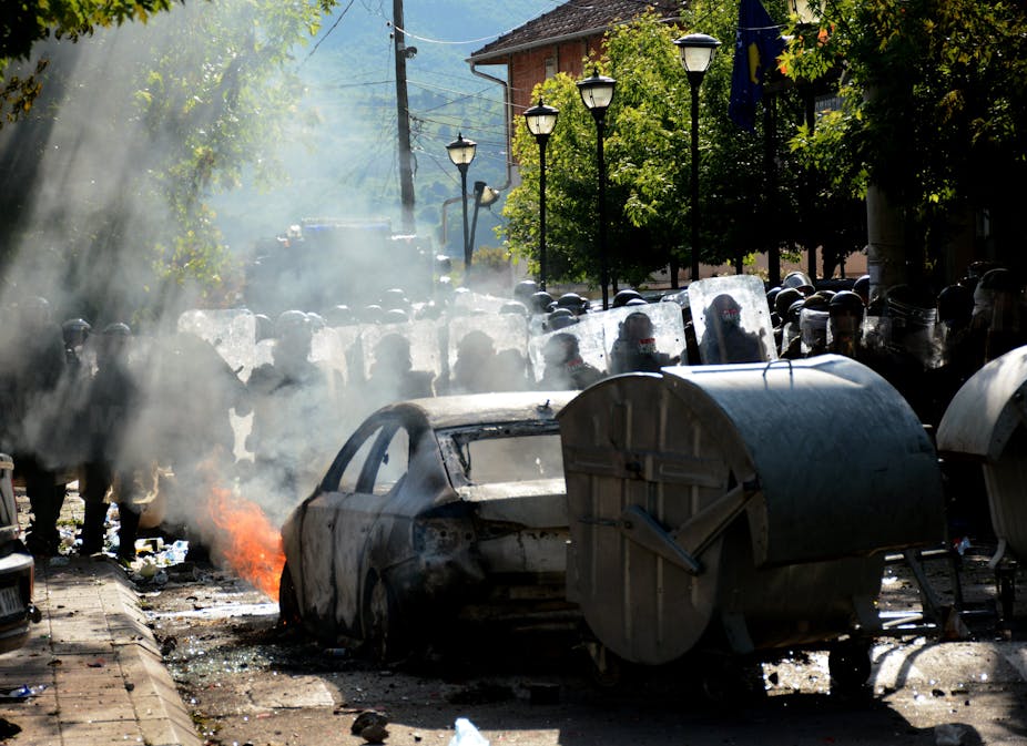 Des policiers anti-émeute devant des véhicules en train de brûler