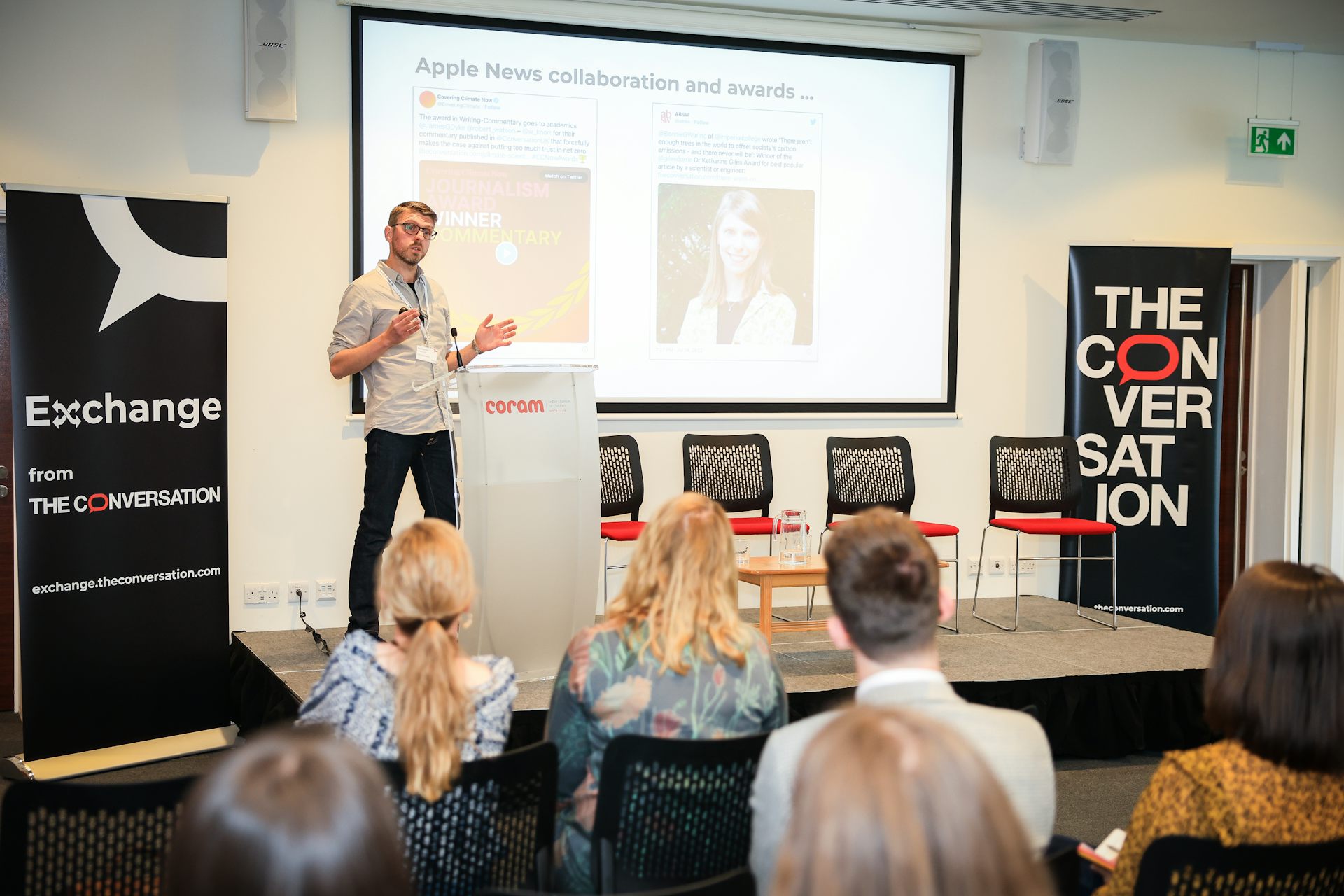 Paul Keaveny stands on a raised platform flanked by The Conversation-branded banners talking to the audience