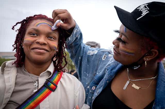 A woman draws a rainbow on her friend's face