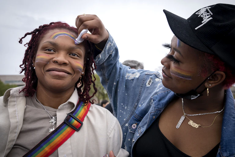 A woman draws a rainbow on her friend's face