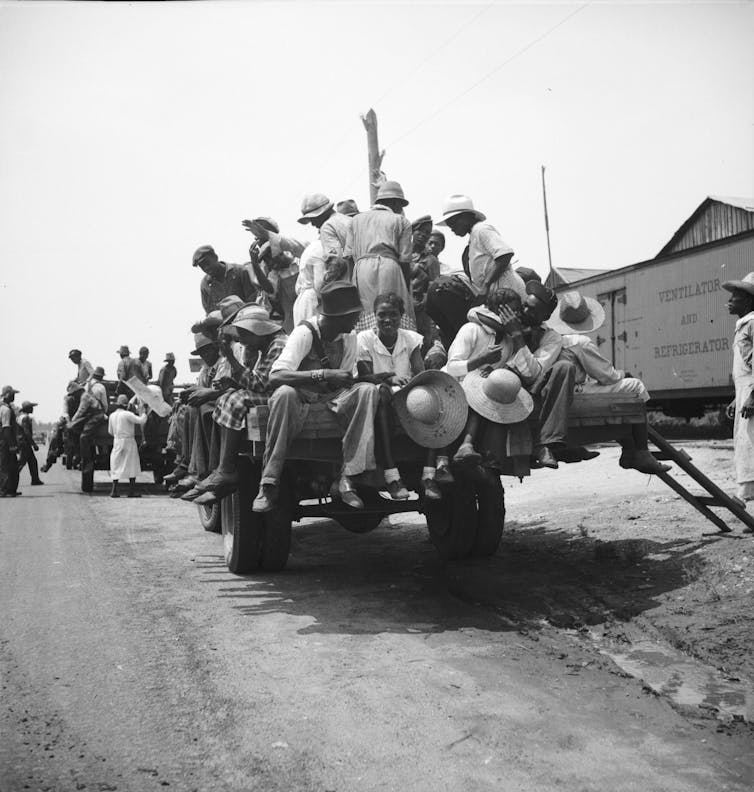 African American men and women sitting and standing on the back of a truck.