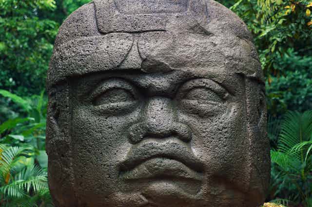A huge head carved of stone sits in a jungle.